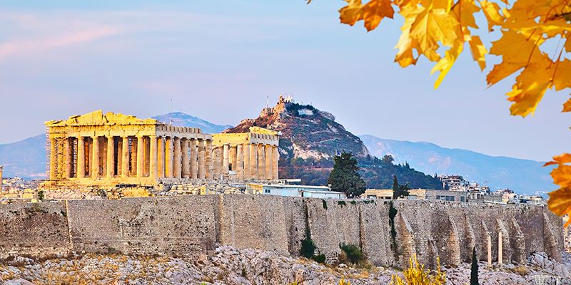 View of the Acropolis with the Parthenon in Athens, Greece, under a blue sky with autumn leaves in the foreground.