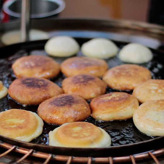 Golden, crispy pancakes frying on a round griddle, with some uncooked ones in the background.
