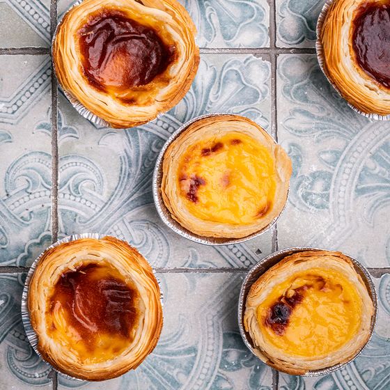 Four Portuguese egg tarts with golden-brown tops on decorative blue and gray patterned tiles.