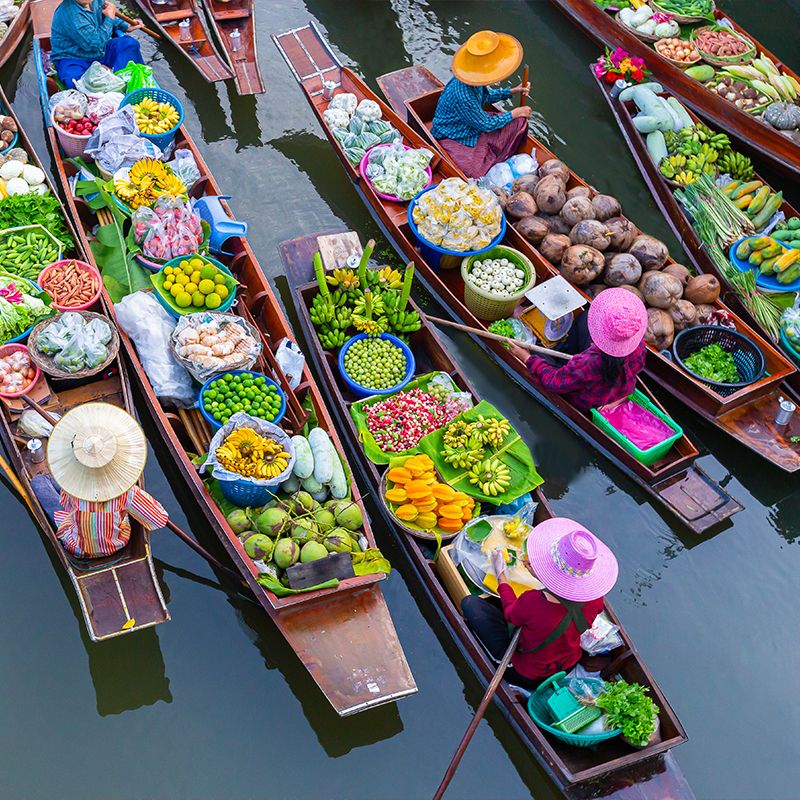 Aerial view of vibrant floating market with vendors in colorful hats selling fruits and vegetables from wooden boats on a calm river.
