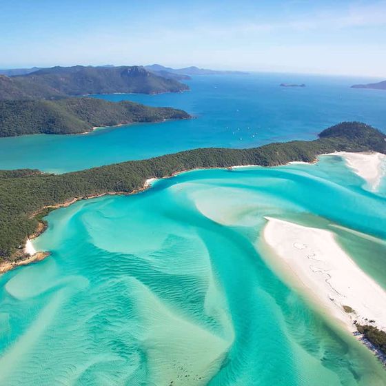 Aerial view of a coastal area with turquoise waters, white sandbars, and lush green islands under a clear blue sky.