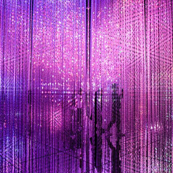 A dazzling room filled with vertical strands of purple and pink LED lights, creating a vibrant, immersive digital art installation.