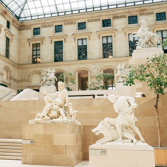 Spacious museum gallery with large sculptures of figures and horses, surrounded by neoclassical architecture and indoor trees.