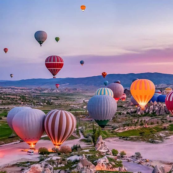Colorful hot air balloons floating over a scenic landscape with rocky formations at sunrise.