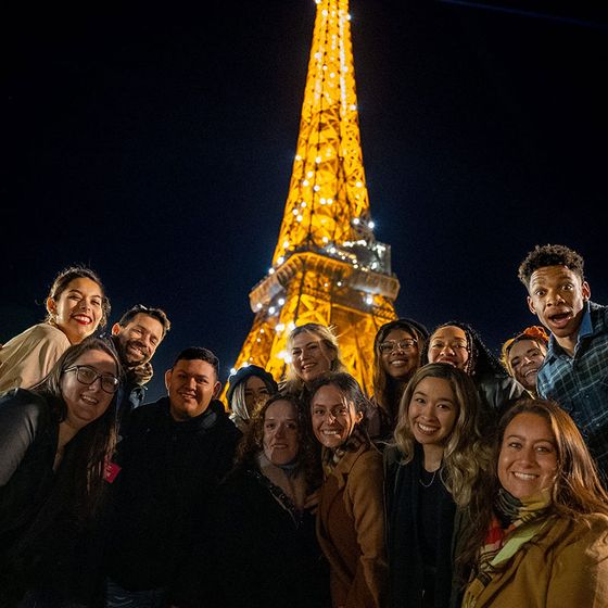 A group of people smiling and posing in front of the illuminated Eiffel Tower at night.