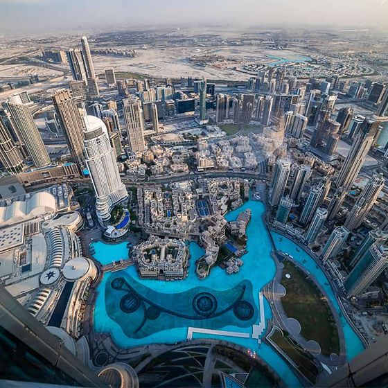 Aerial view of a cityscape with skyscrapers, a large turquoise pool, and intricate roads, showcasing an urban environment.
