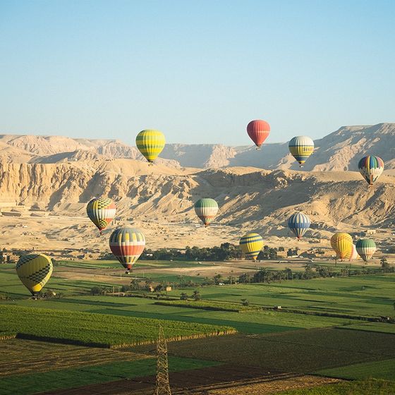 Colorful hot air balloons floating over a lush green landscape with sandy mountains in the background under a clear blue sky.