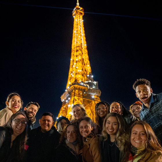 A group of people smiling in front of the illuminated Eiffel Tower at night.