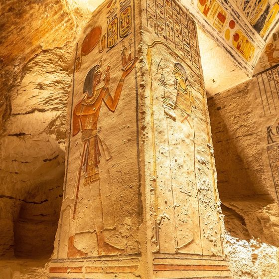 Ancient Egyptian pillar adorned with colorful hieroglyphs and figures, located in a softly lit historical chamber with stone walls.
