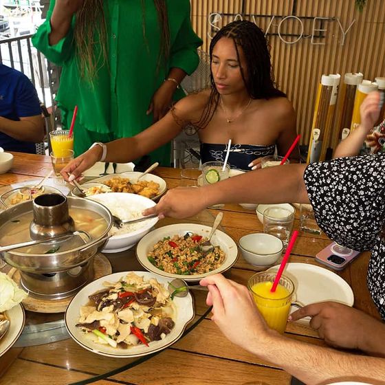A group of people enjoying a meal at a restaurant table with dishes like salad, chicken, and drinks. A steamer is placed on the table.