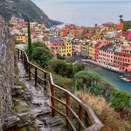 Cliffside path overlooking colorful buildings and a harbor in Vernazza, Italy, with the sea in the background.