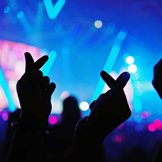Silhouetted hands making heart gestures at a lively concert, vibrant blue and pink lights illuminating the background.