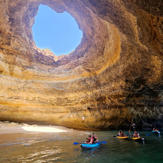 Kayakers exploring a sunlit sea cave with a large opening above, revealing a clear blue sky.