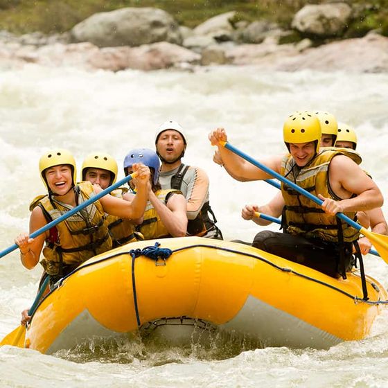 A group of six people in helmets and life vests rafting through whitewater rapids in a yellow inflatable boat.