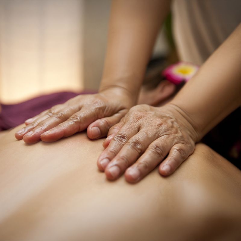 Hands giving a relaxing back massage, with soft lighting and a flower tucked by the person's ear.