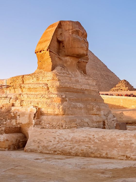 The Great Sphinx of Giza with a pyramid in the background, bathed in warm sunlight under a clear blue sky.