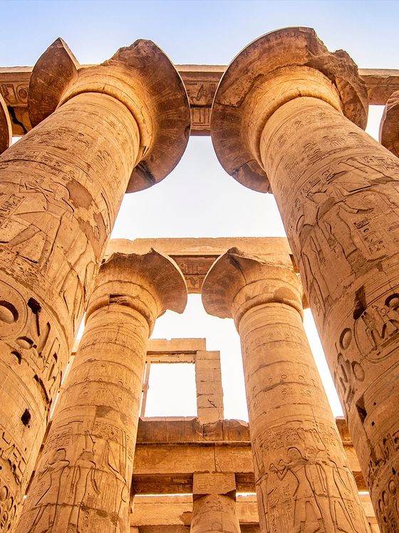 Low-angle view of ancient Egyptian columns with hieroglyphs under a clear blue sky at Karnak Temple.