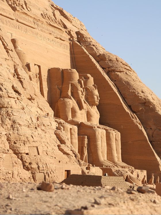 The Great Temple at Abu Simbel with four colossal seated statues carved into a sandstone cliff, under a clear blue sky.