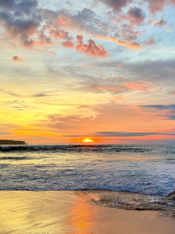 A stunning sunset over a beach with vibrant orange, pink, and blue hues in the sky, gentle waves lapping the shore.