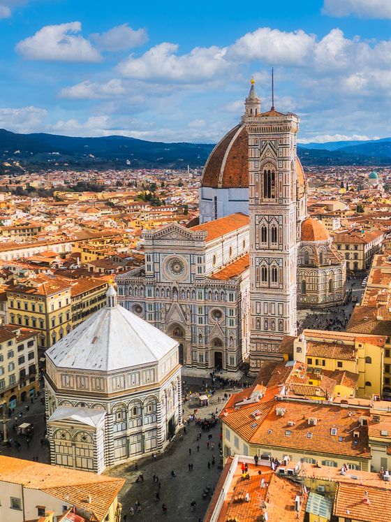 Aerial view of Florence's Cathedral of Santa Maria del Fiore with its iconic dome and campanile, surrounded by historic buildings under a blue sky.