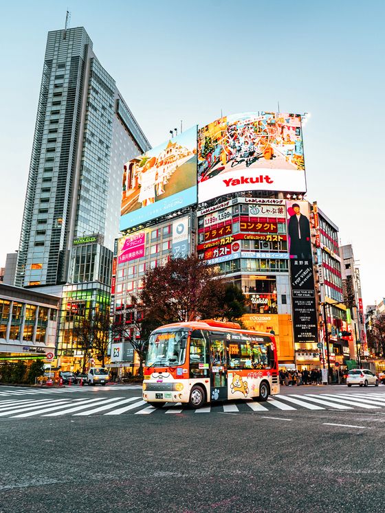 A vibrant city intersection with a colorful bus, large digital billboards, and tall buildings during daylight.