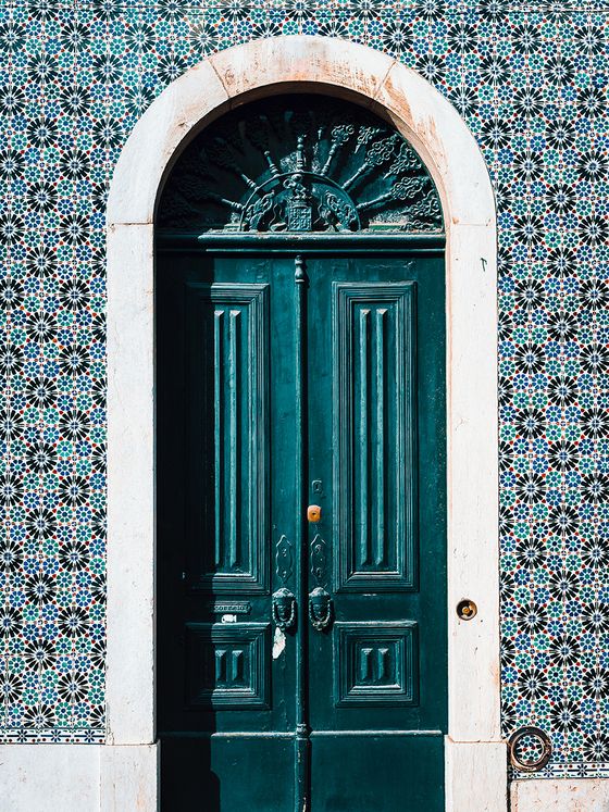 Vintage green double doors set in a tiled wall with intricate geometric patterns and a decorative stone arch above.