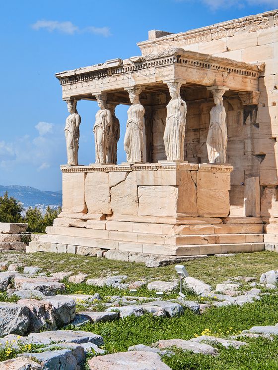 The Erechtheion's Porch of the Caryatids, featuring six female-shaped columns, on the Acropolis in Athens under a clear blue sky.