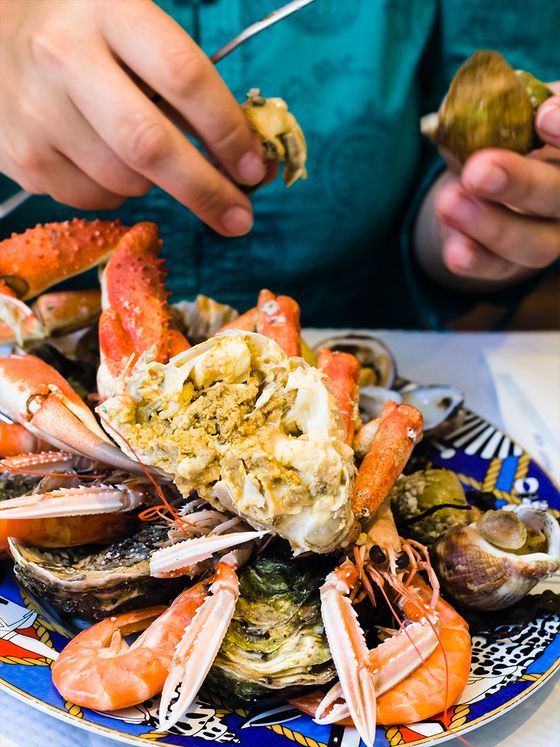 A person preparing to eat a colorful seafood platter with crab legs, shrimp, and clams on a decorative plate.