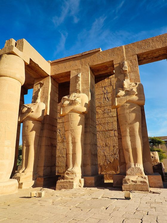 Ancient Egyptian temple with massive stone columns and carvings under a clear blue sky.