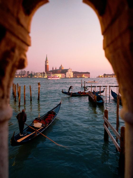 Gondolas on Venice's Grand Canal at sunset, viewed through an archway, with the San Giorgio Maggiore church in the background.
