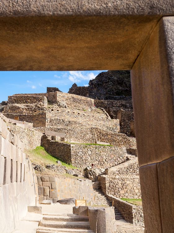 View through a stone doorway of ancient terraced ruins under a blue sky at Ollantaytambo, Peru.