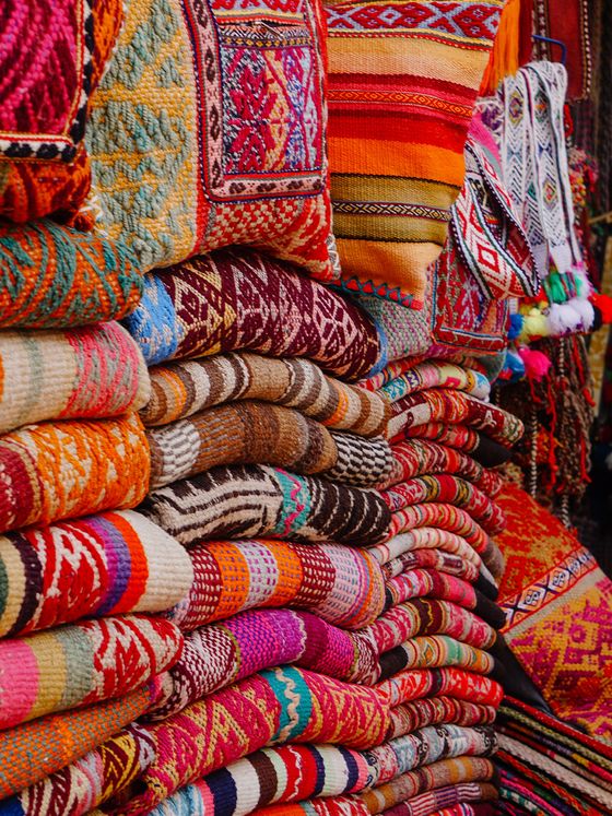 Stacks of colorful woven textiles with intricate patterns, featuring bold reds, oranges, and other vivid hues.