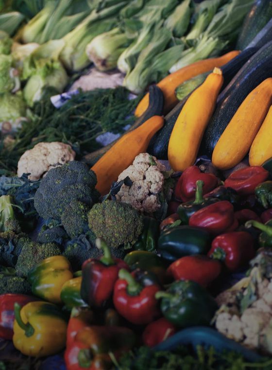 A colorful assortment of vegetables including zucchini, bell peppers, broccoli, and cauliflower, displayed at a market stall.