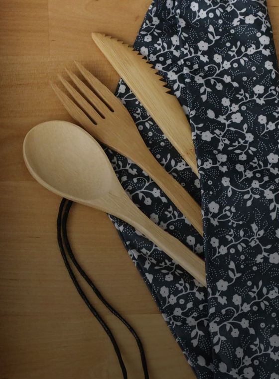 Wooden spoon, fork, and knife partially tucked into a floral-patterned fabric bag on a wooden surface.