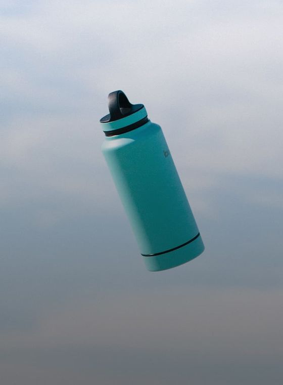 A turquoise water bottle with a black lid is floating against a light blue sky background.