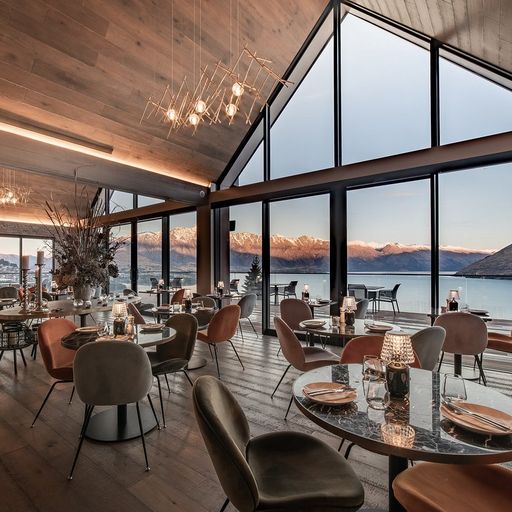 Elegant restaurant with modern decor, large windows offering a stunning mountain and lake view, and tables set for dining.