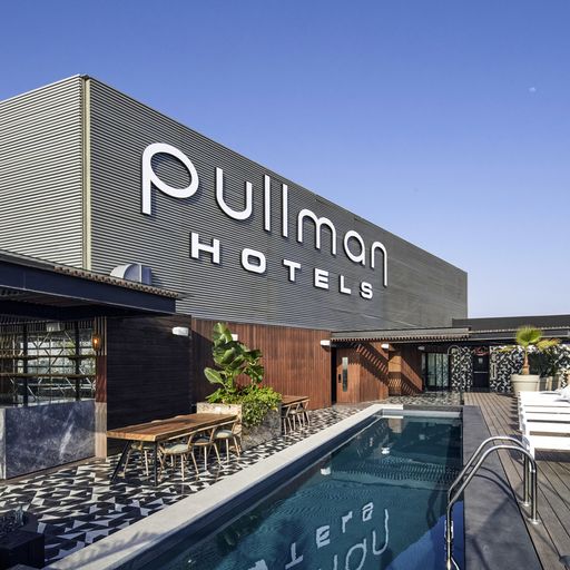Rooftop pool area at Pullman Hotels with lounge chairs, tables, and a clear blue sky.