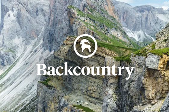Mountain landscape with rugged peaks, grassy foreground, and wildflowers, featuring the "Backcountry" logo and a mountain goat icon overlay.