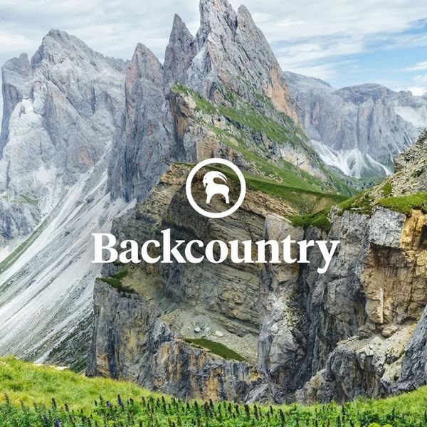Mountain landscape with rugged peaks, grassy foreground, and wildflowers, featuring the "Backcountry" logo and a mountain goat icon overlay.