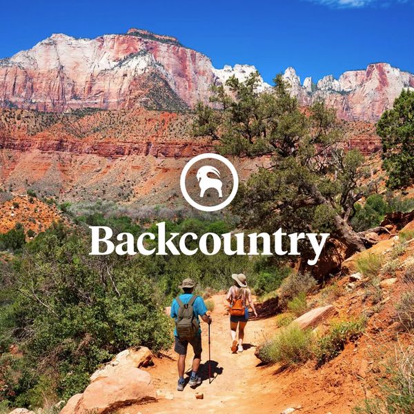 Two hikers on a scenic trail with red rock formations and blue sky, featuring the word "Backcountry" and a mountain goat logo at the center.