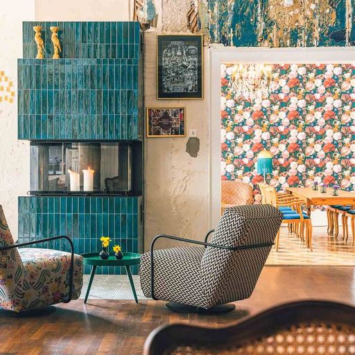 Eclectic living room with patterned armchairs, a teal tiled fireplace, and a view into a floral wallpapered dining room.