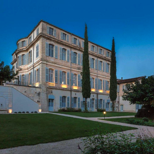 Elegant three-story building with large windows, surrounded by manicured lawns and tall cypress trees, under a clear evening sky.