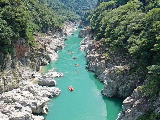 Aerial view of a turquoise river cutting through a rocky gorge, with several red rafts floating amidst lush greenery.