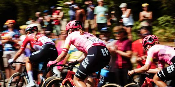 Cyclists in pink jerseys race on a road, surrounded by a blurred crowd of spectators.