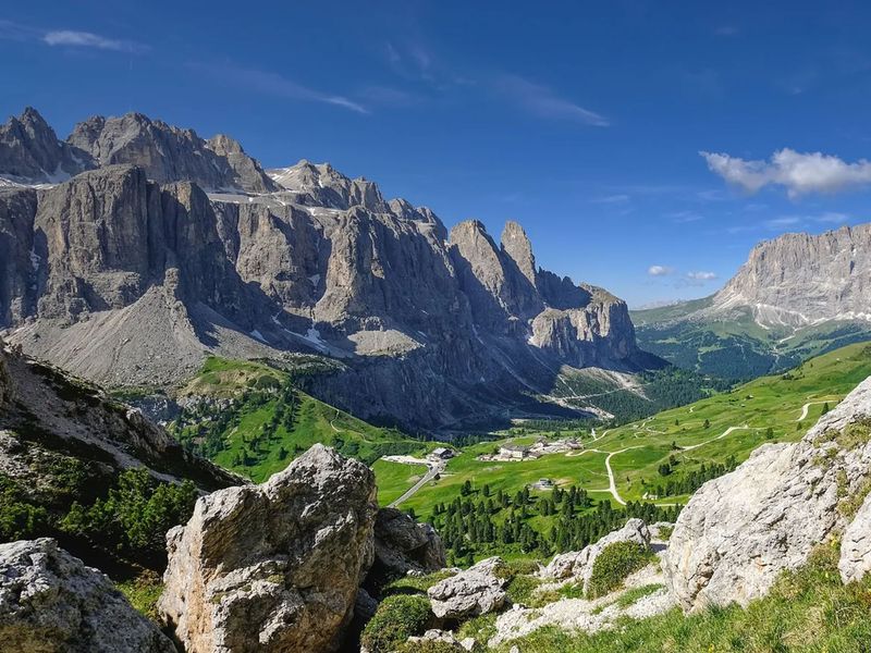 Mountain landscape with rocky peaks, lush green valleys, and a clear blue sky. Scenic view of the Dolomites in summer.