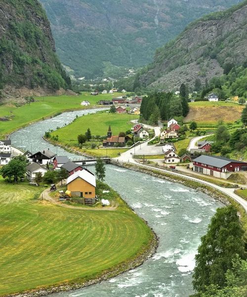 A small village with colorful houses nestled in a lush green valley, a winding river, and mountains in the background.