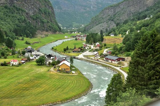 A small village with colorful houses nestled in a lush green valley, a winding river, and mountains in the background.