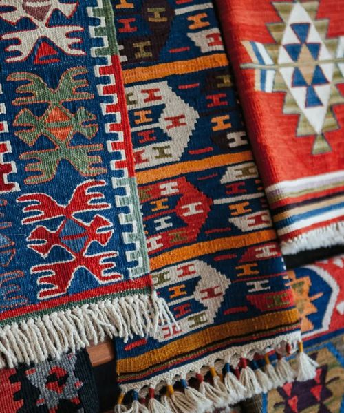 Colorful woven tapestries hanging in a row, featuring intricate geometric patterns and tribal designs in red, blue, and yellow hues.