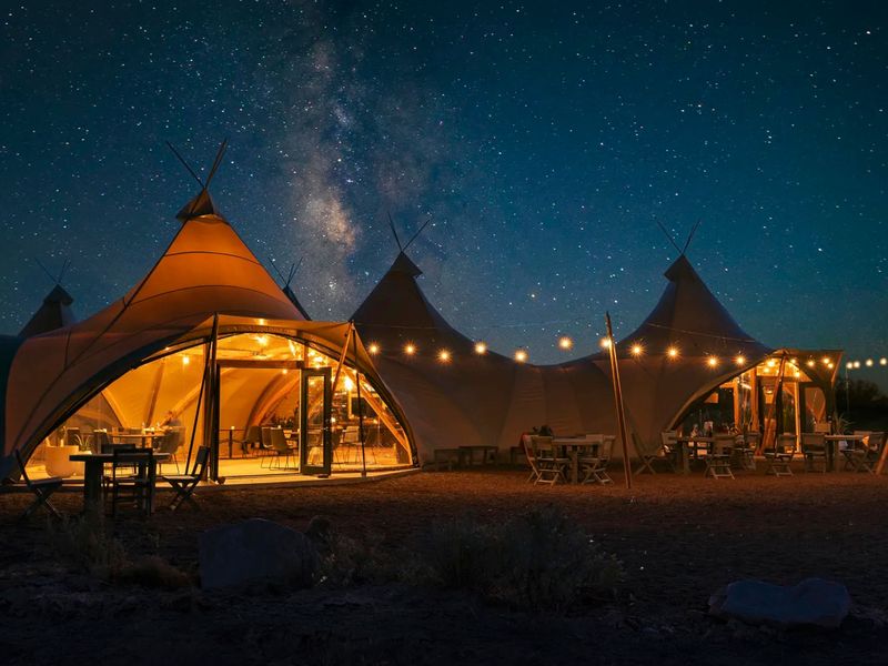 Illuminated tents under a starry night sky with string lights, set in a desert landscape.
