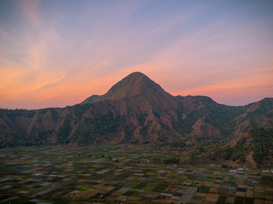 A picturesque mountain at sunset with a gradient sky and a patchwork of fields in the foreground.